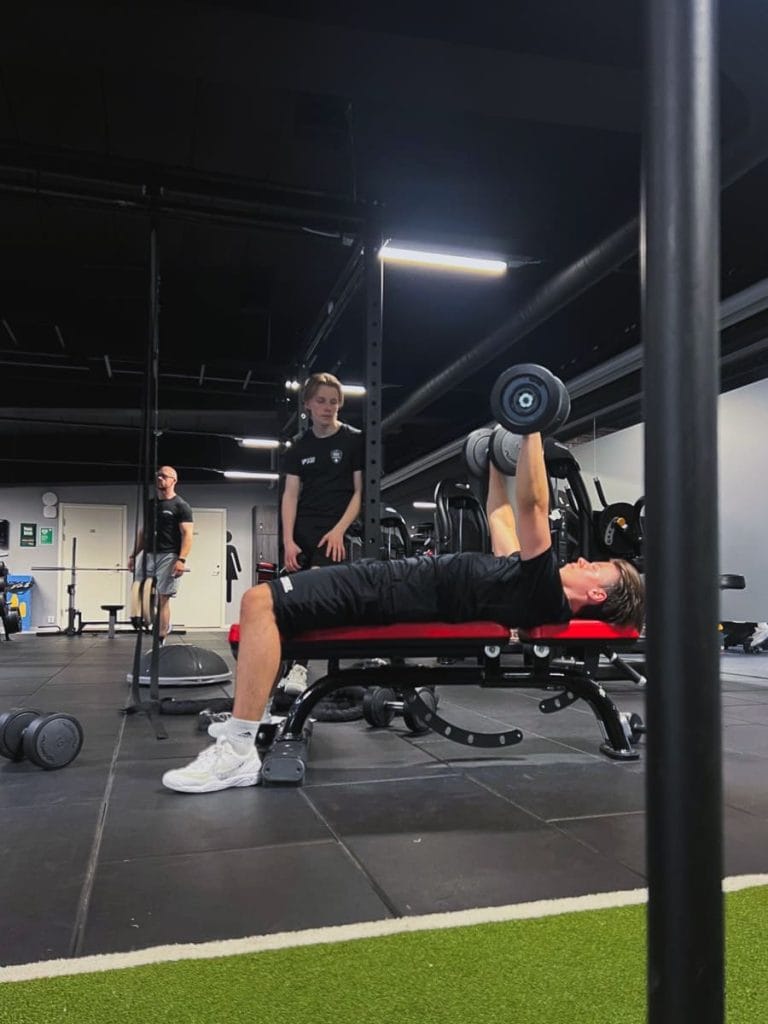 Ulf Berg coachar en klient som tränar med hantlar på bänk i gymmet – personlig träning i Örnsköldsvik